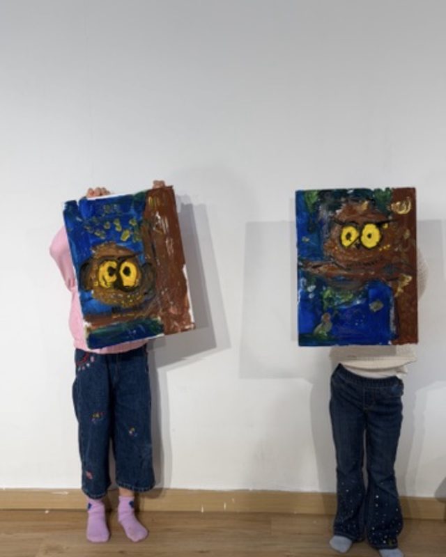 Two kids holding up their owl paintings