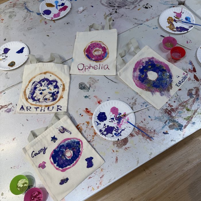 Hand-painted donut tote bags on a messy art table