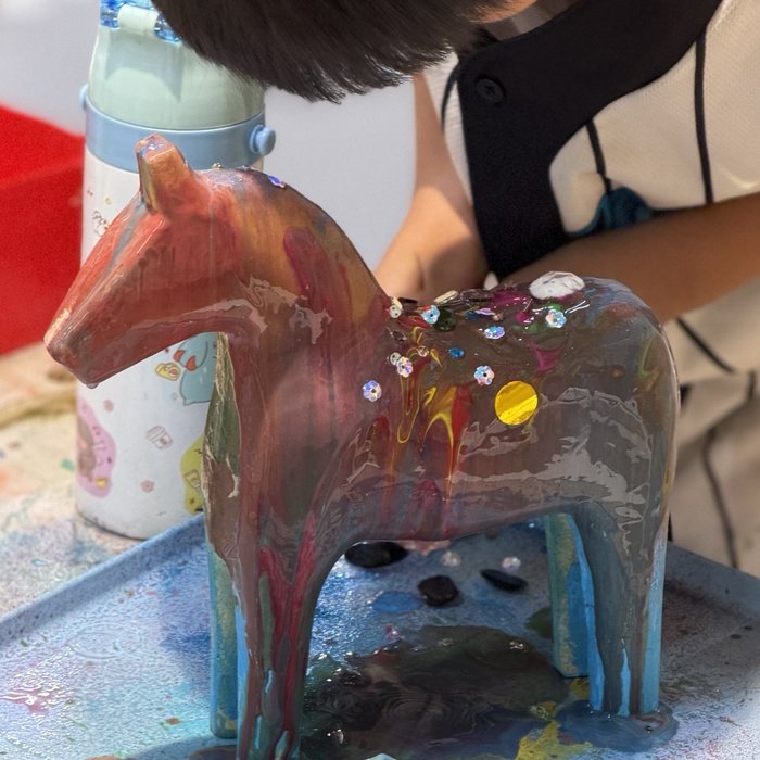 Boy decorating a pour-painted wooden horse with sequins