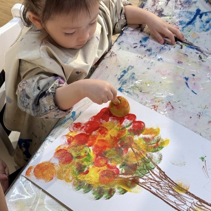 Toddler sponge-stamping an autumn tree
