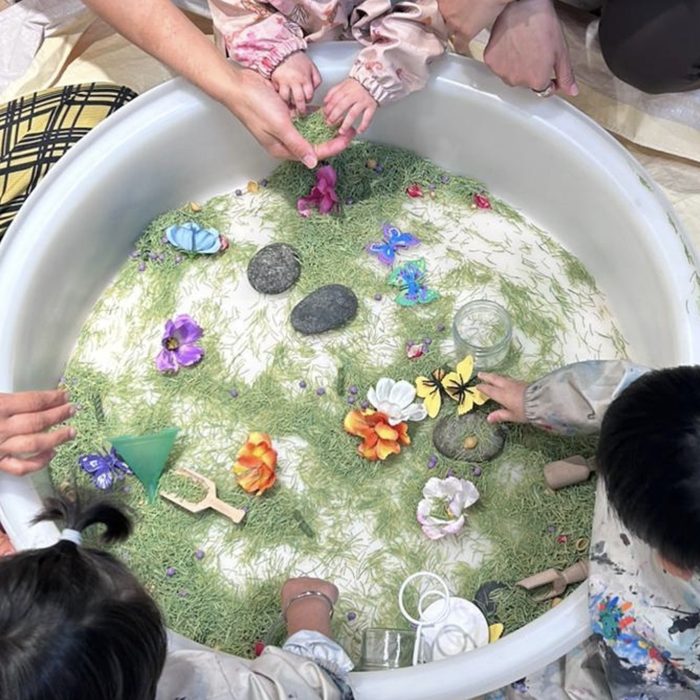 Toddlers exploring a garden sensory tub with butterflies, flowers and stones
