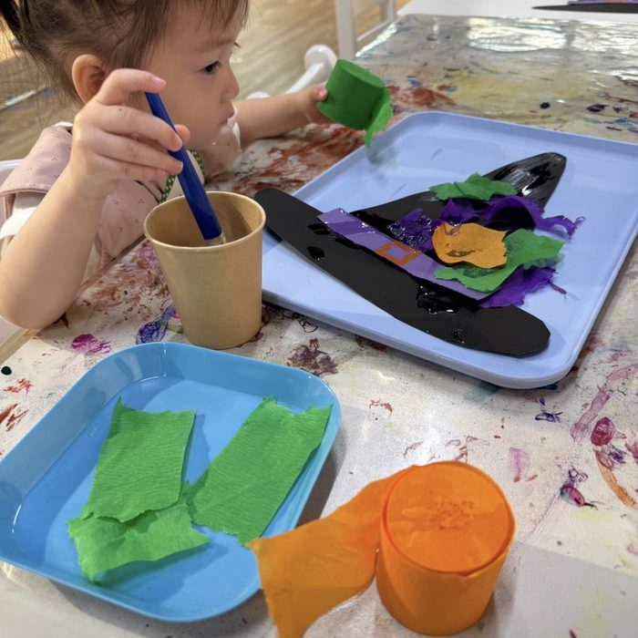 Toddler gluing tissue paper onto a witch hat