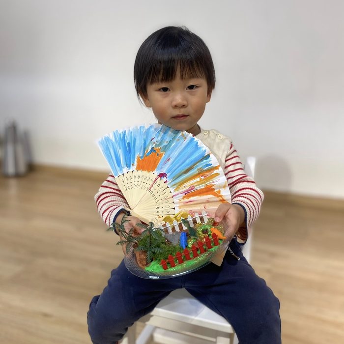 Toddler holding a painted fan and a dinosaur garden craft