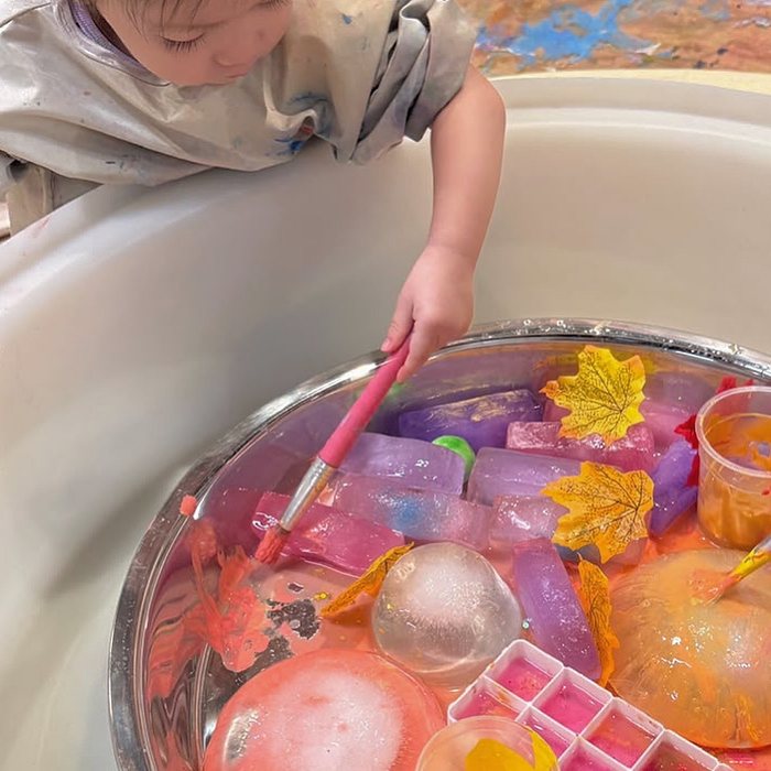 Toddler painting colourful ice blocks in a tray