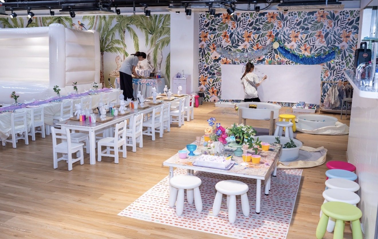 Jungle Arts party room set up with white tables, flower wall and bouncy castle